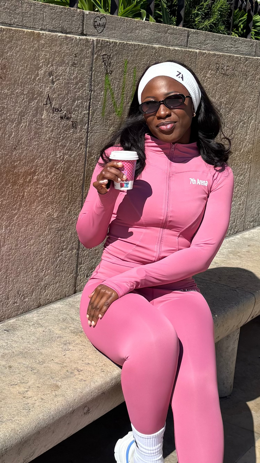 Person in a pink outfit sitting on a bench holding a coffee cup.