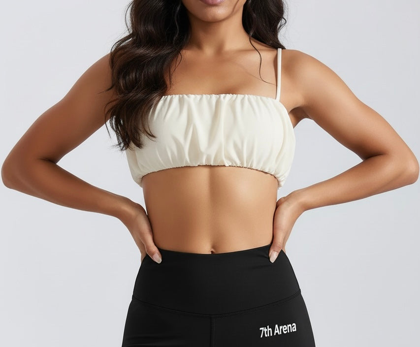 Woman wearing a off white sports bra / top and black leggings with '7th Arena' branding on a light gray background