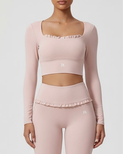 Person wearing a pink long-sleeve athletic cropped top and leggings with a logo on a light gray background