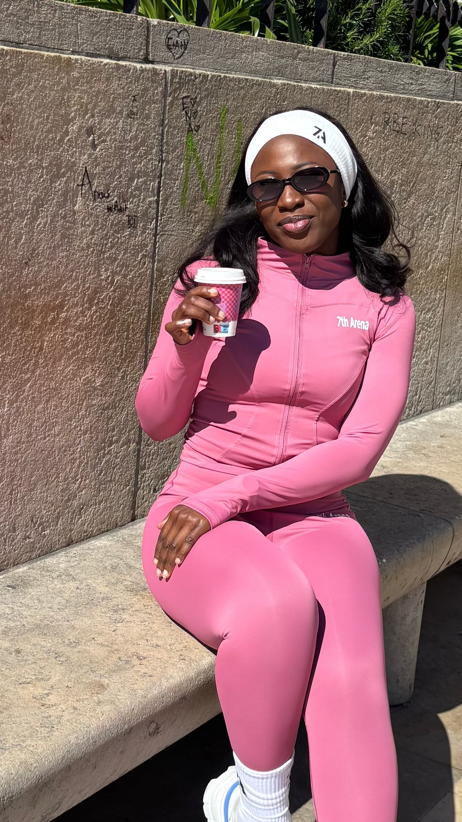 Person in a pink outfit sitting on a bench holding a coffee cup.