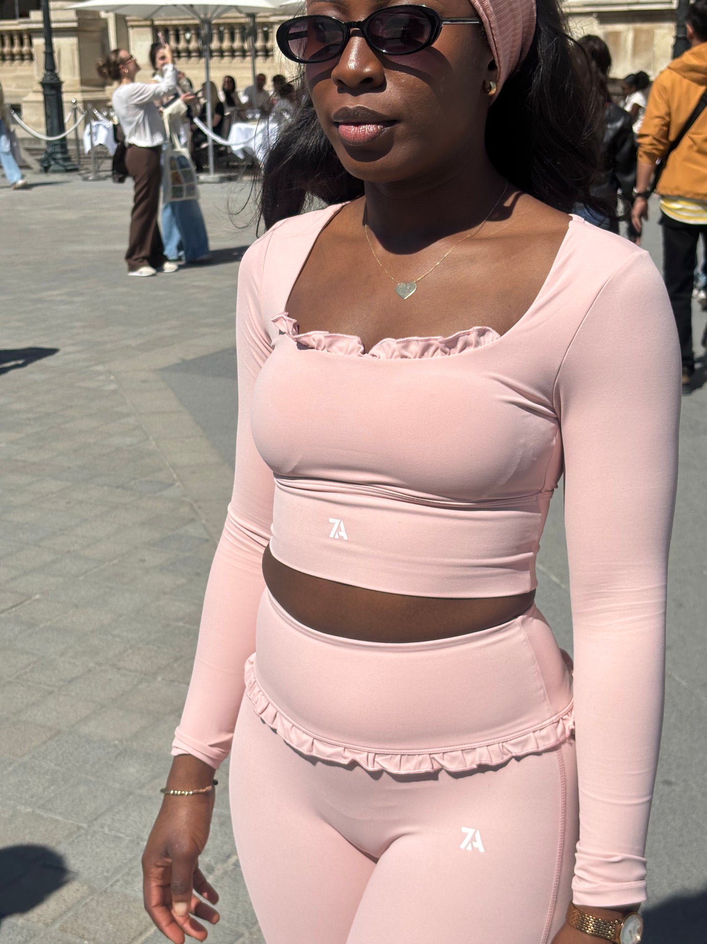 Woman wearing a light pink outfit with ruffled details on a blurred outdoor background
